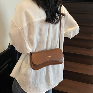 Sac sous le bras minimaliste en cuir marron avec rabat ondulé porté par un mannequin