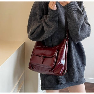 Detail shot of a glossy burgundy faux leather crossbody bag with a magnetic buckle pocket