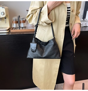 Close-up of black woven shoulder bag with a small square pouch on a stylish trench coat