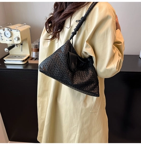 Close-up of a black woven leather bucket bag with a unique twisted shoulder strap