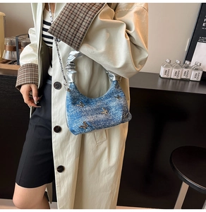 Détail du sac bandoulière en denim bleu avec papillons argentés et poignée plissée