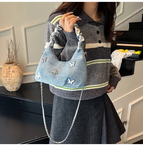 Détail du sac seau en denim bleu clair avec papillons argentés et bandoulière chaîne