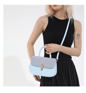 Blue saddle bag with grey woven texture flap and gold horseshoe clasp on black dress