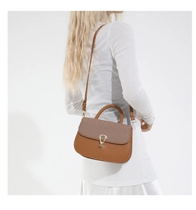 Detail of caramel brown saddle bag featuring woven texture and golden handle ring