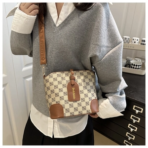 Close-up of checked bucket bag with brown leather details and woven shoulder strap