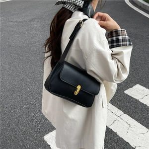 Minimalist black leather underarm bag with gold metal buckle shown on model in street view