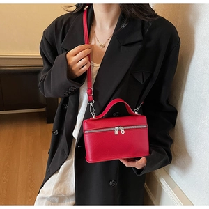 Detail of red leather crossbody bag with litchi texture on a model in black suit