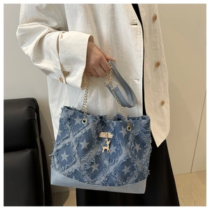 Detail of blue denim tote bag featuring white star prints and a gold deer pendant