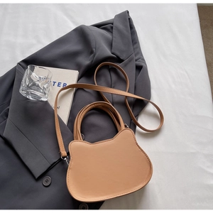Detail of cute cat-shaped crossbody bag in light brown leather on a grey blazer background