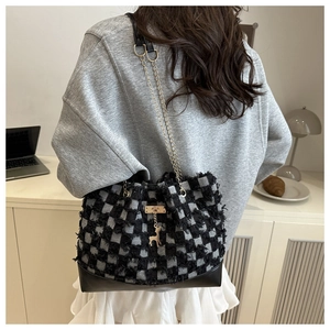 Close-up of black and white checkered tweed tote bag with fringe and deer pendant