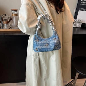 Sac à main en denim bleu avec papillons argentés porté sur un manteau beige chic