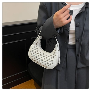 Dettaglio borsa a mezzaluna bianca con borchie argentate su sfondo blazer grigio