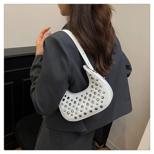 Vista laterale di una borsa a mezzaluna bianca con borchie argentate su un blazer grigio