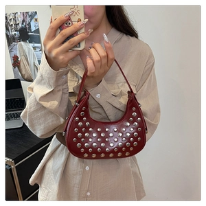 Dettaglio di una borsa hobo in pelle bordeaux con borchie argentate indossata da un modello