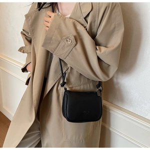 Detail of black lychee grain leather saddle bag on camel trench coat strap view