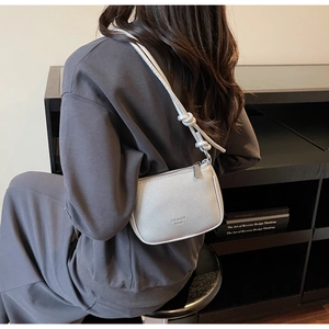 Detail of silver crossbody bag featuring litchi grain leather and knot strap design