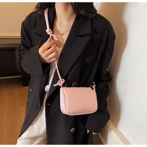 Pink lychee grain leather crossbody bag with knot strap detail and logo shown on model
