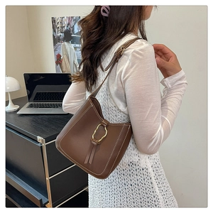 Détail d'un sac porté épaule en cuir marron avec anneau doré, glands en cuir et coutures