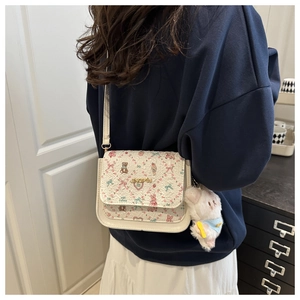 Detail of a beige crossbody bag with cartoon bear prints and plush puppy pendant