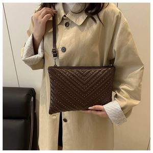 Détail du sac rétro matelassé marron avec clous argentés porté sur un trench-coat