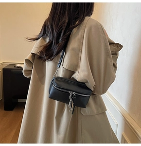 Detail of a black leather crossbody box bag styled on a trench coat with metal pendant