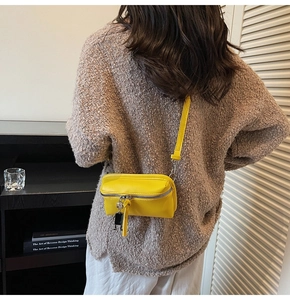 Detail of yellow pebbled leather crossbody bag with a metallic robot charm accessory