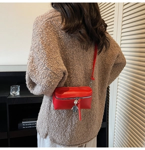 Detail of red leather box bag with silver zipper and unique robot charm hanging on side