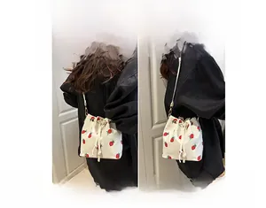 Close-up of strawberry print canvas bucket bag showing crossbody and shoulder strap styles