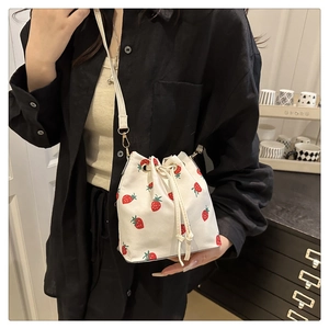Detail of white drawstring canvas bucket bag with strawberry print and leather strap