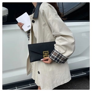 Close-up of black envelope handbag with gold buckle and stylish trench coat details