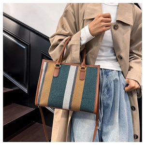 Vertical striped patchwork tote bag in green and beige shown held by a model in a trench coat