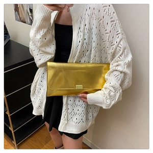 Détail d'une pochette rectangulaire dorée métallisée avec un fermoir en métal poli chic