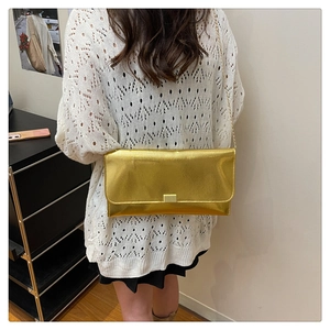 Détail d'une femme portant le sac enveloppe doré avec bandoulière à la chaîne