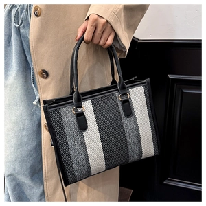 Close-up of contrast striped tweed tote bag with black leather handles and gold ring detail