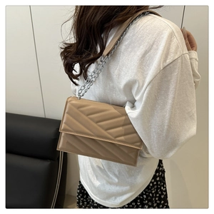 Détail d'un sac à bandoulière matelassé marron clair avec chaîne porté par un mannequin