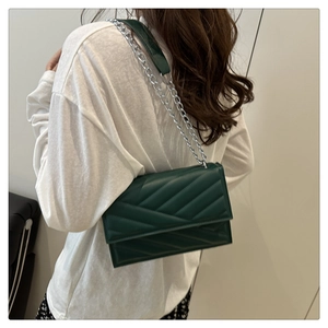 Gros plan d'un sac bandoulière matelassé vert foncé avec chaîne porté par un mannequin