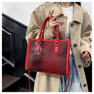 Dettaglio di una borsa tote rossa con trama a coccodrillo portata con un trench beige