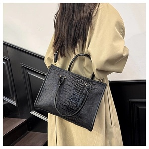Dettaglio della borsa tote nera a trama coccodrillo portata a spalla su cappotto beige