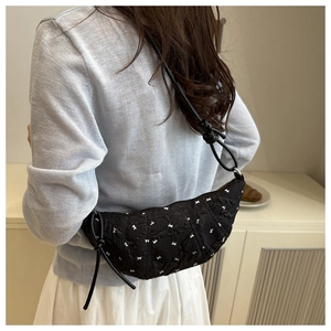 Close-up of black quilted dumpling bag with white bow embroidery and knotted strap detail