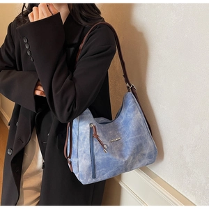 Close-up of blue textured tote bag with metal FASHION logo and tassel zipper detail