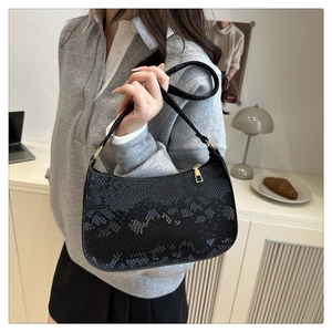 Close-up of black faux snake skin texture and gold zipper on a fashion baguette bag