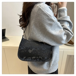 Détail du sac baguette noir avec gaufrage serpent et fine bandoulière sur l'épaule