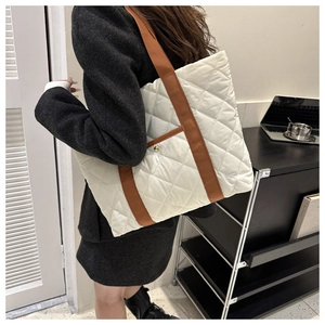 Detail of a large white quilted tote bag with brown straps worn on a shoulder