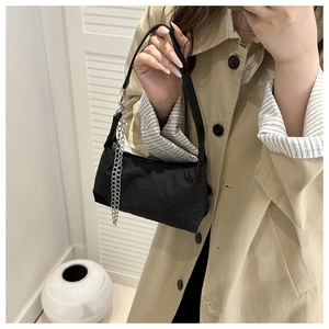 Detail of minimalist black nylon crossbody bag with metal chain strap on model
