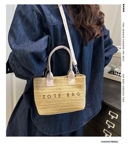 Model wearing a straw tote bag with cream leather straps and TOTE BAG embroidery