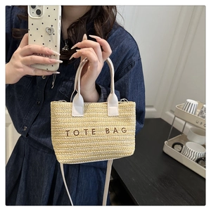 Detail of hand-woven straw tote bag with white leather handles and embroidered logo