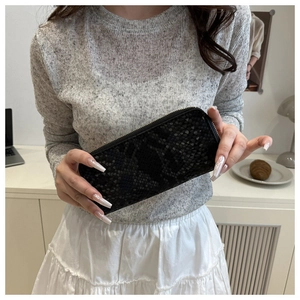 Close-up of black snake pattern long wallet with zipper held by a model in a home setting