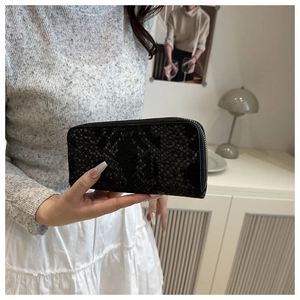 Close-up of black snakeskin pattern wallet held by a model in a modern home setting