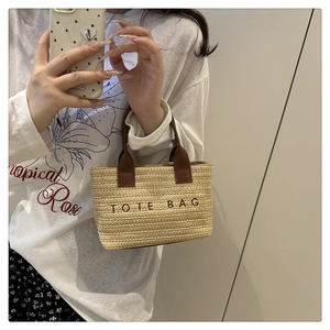 Détail d'un sac cabas en paille tressée avec texte brodé et anses en cuir marron