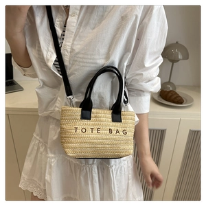 Détail d'un sac cabas en paille avec poignées en cuir noir et broderie TOTE BAG chic